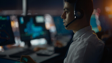 Male Air Traffic Controller with Headset Talk on a Call in Airport Tower. Office Room is Full of Desktop Computer Displays with Navigation Screens, Airplane Departure and Arrival Data for the Team.