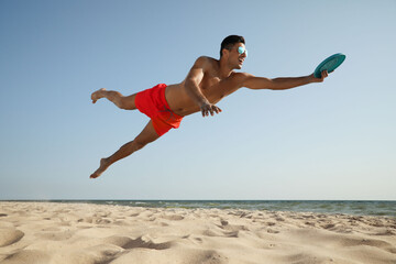 Sportive man jumping and catching flying disk at beach © New Africa