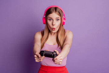 Portrait of funny crazy lady hold gamepad play console videogame wear headphones pink top on violet background © Tetiana