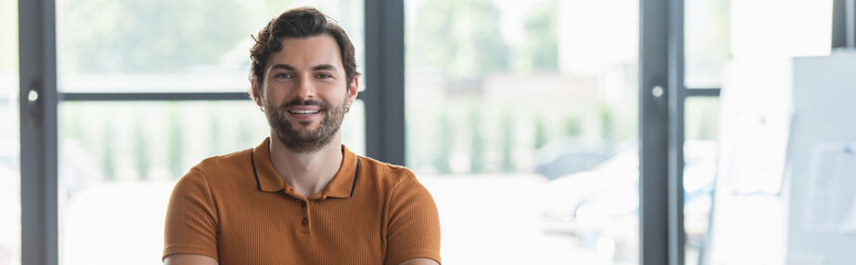 Cheerful businessman smiling at camera in office, banner