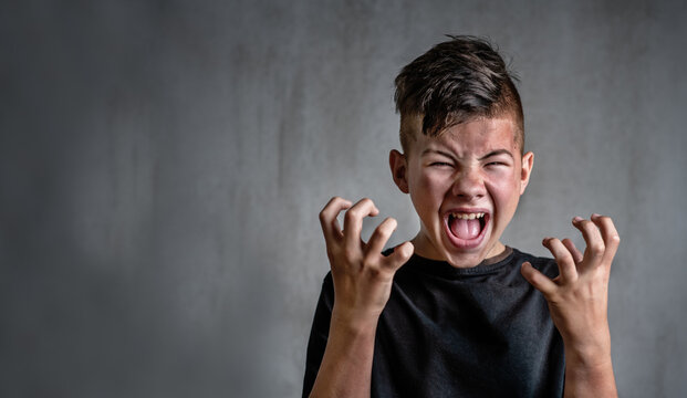 Teen boy screaming in anger on dark background