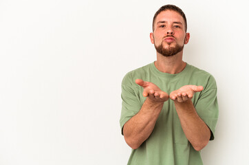 Young caucasian man with diastema isolated on white background folding lips and holding palms to send air kiss.