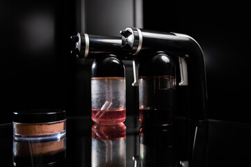 A close-up of the instant tanning equipment. Gun spraying paint for leather, brush and matting body powder on a black background.