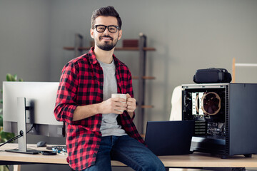 Portrait of nice attractive smart clever cheerful guy sitting on table drinking beverage at work...