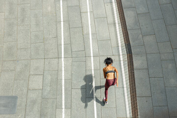 Young biracial woman in stylish sportswear runs along empty stadium track upper view. Development and achievement concept