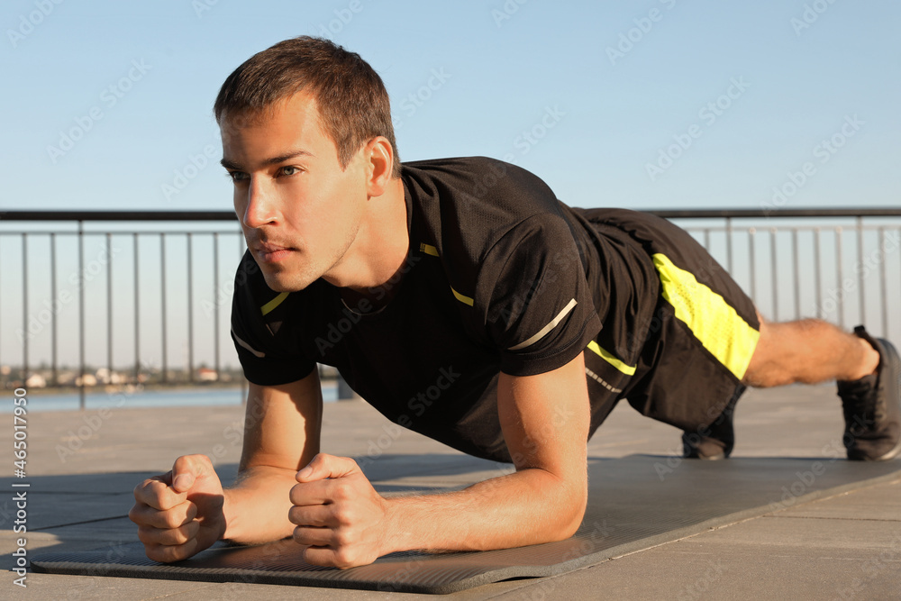 Poster Sporty man doing plank exercise on mat outdoors