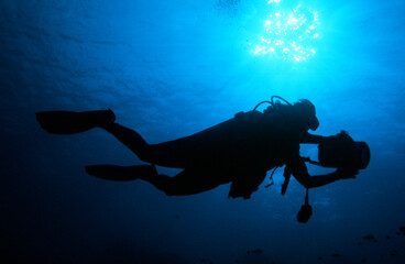 A Scuba Diver Exploring the Ocean Silhouetted by the Sun with a Video Camera