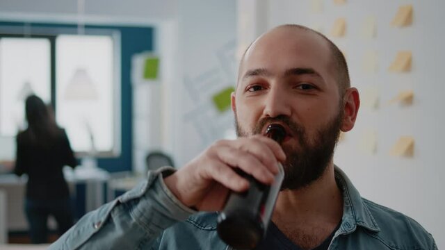 Portrait of businessman holding bottle of beer after work in office for fun activity with colleagues. Cheerful person drinking alcoholic beverage while celebrating with friends after hours