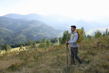 Tourist with backpack and trekking poles hiking through mountains, space for text