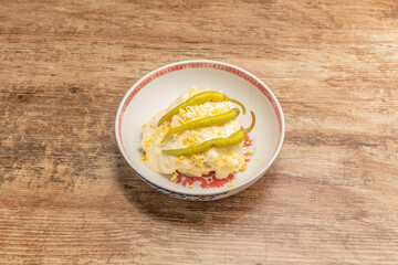 bowl with Russian salad with boiled egg, mayonnaise sauce and piparras on top