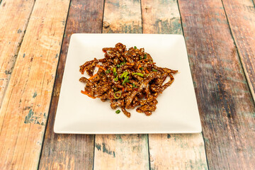 Fototapeta na wymiar Chinese recipe of caramelized beef strips with grated carrots, chopped vegetables and semisalums of sesame and poppy on white plate