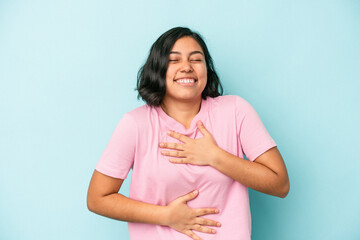 Young latin woman isolated on blue background laughs happily and has fun keeping hands on stomach.