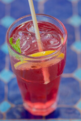 Close up of a colorful cold beverage, with a slice of lemon and a basil leaf 