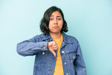 Young latin woman isolated on blue background showing a dislike gesture, thumbs down. Disagreement...