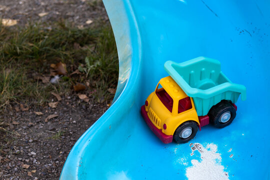 plastic toy truck on bench,wooden fence,swing for kids or blue old slide,peeled paint.one left toy for kid,little boy,abandoned.forgotten toy awaiting the child owner.orange,red,blue.autumn sunny day,