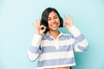 Young latin woman isolated on blue background cheerful and confident showing ok gesture.