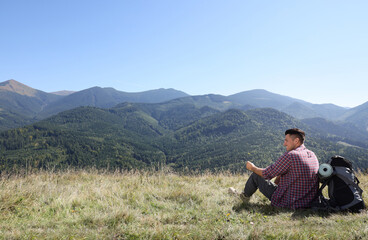 Naklejka na ściany i meble Tourist with backpack sitting on ground and enjoying view in mountains