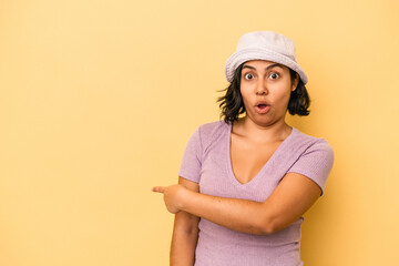 Young latin woman isolated on yellow background smiling and pointing aside, showing something at blank space.