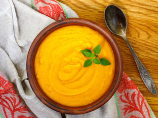 traditional vegetarian spicy red lentil soup in clay bowl on the wooden background and textile napkin with spoon top view close-up