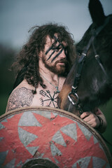 Naklejka na ściany i meble Medieval warrior berserk Viking portrait with tattoo on skin, cuts on body and braids in hair with weapons to attacks enemy. Concept historical photo