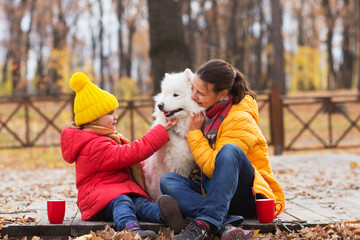 Fototapeta premium mom and child daughter walk with a dog and drinking hot tea from thermos in autumn park. 