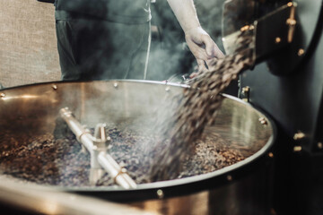 Obraz premium Man pouring coffee beans into the roaster machine. Roasting process of fresh coffee beans in a coffee shop