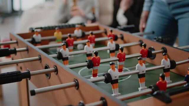 Close up of colleagues playing at foosball table after work. Workmates using board to play football and to score goal while enjoying drinks and snacks at celebration after hours
