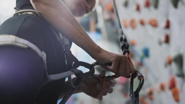 Sport athletic woman secures the safety rope, carabiner hook. Attaches the belay to the carabiner. Climbing solo in indoor gym. Hobby in the city, healthy lifestyle. Slow motion