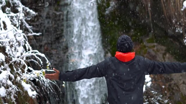 Portrait of an Indian man enjoying snowfall during the winter and raising his arms at Jana waterfall in Kullu, Himachal Pradesh, India. Slow motion of man enjoying the snowfall. People enjoying winter