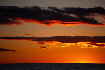 golden light of sunset falling below the horizon with orange glow reflecting off clouds sun setting over Lake Ontario Canada horizontal format room for type