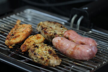 Churrasqueira elétrica com carnes sobre grelha, linguiça, frango e pernil de porco