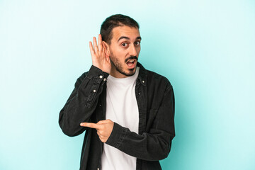 Young caucasian man isolated on blue background trying to listening a gossip.