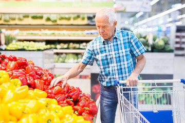 elderly retired man buying bell pepper in grocery section of supermarket