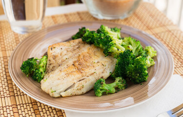fried fillet of sea bass with garnish of broccoli on black warm stone plate