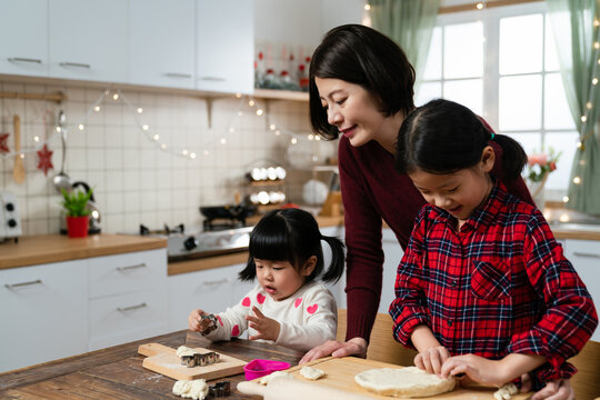 loving asian mom looking at her girls with a smile while they are engaging in making homemade gingerbread cookies for Christmas and new year at home