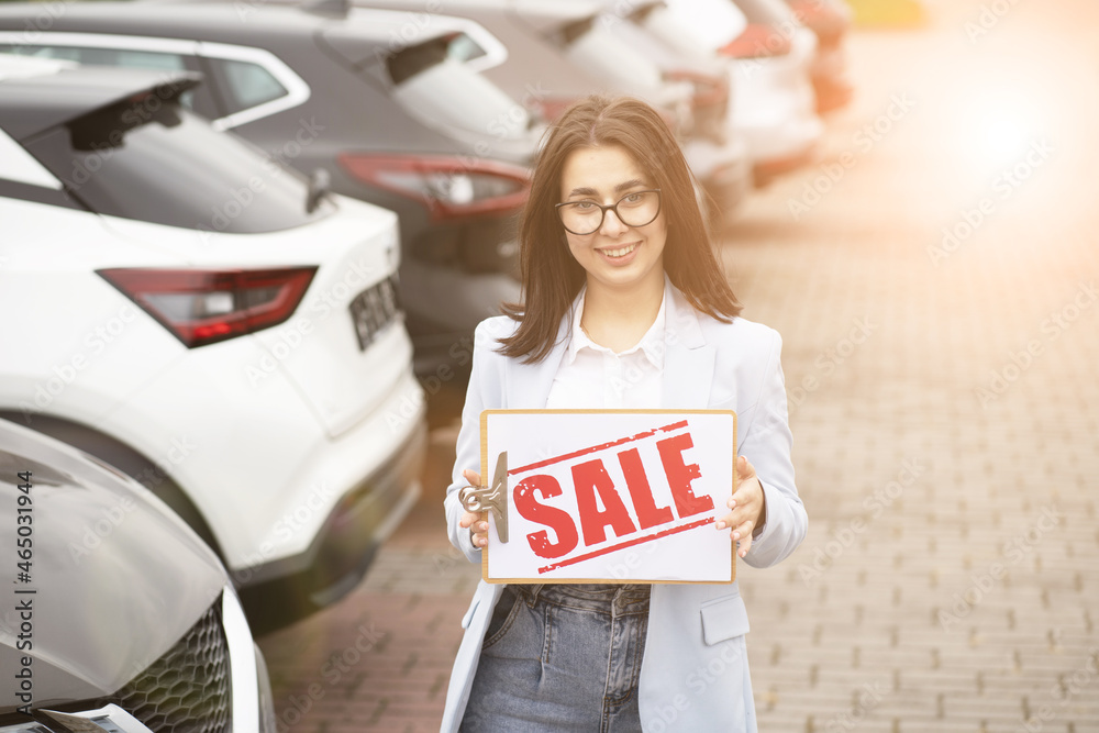 Canvas Prints Smiling woman with sale banner standing among luxury cars