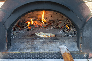 Pita, pizza is cooking in a wood fire in a stone oven