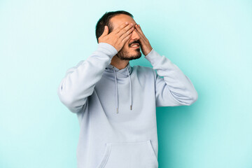 Young caucasian man isolated on blue background afraid covering eyes with hands.