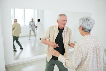 Happy senior couple having fun and dancing during lesson in dance studio with other people