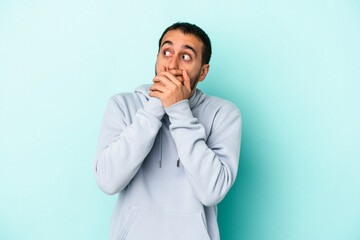 Young caucasian man isolated on blue background thoughtful looking to a copy space covering mouth with hand.