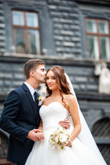 Beautiful young bride with wedding bouquet and groom near old castle before wedding ceremony