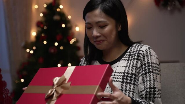asian Japanese woman feeling disappointed with her Christmas gift and forcing smile while pretending to be happy during the holiday celebration at home in the evening