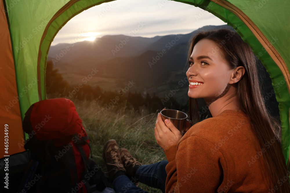 Poster Young woman with drink inside of camping tent in mountains