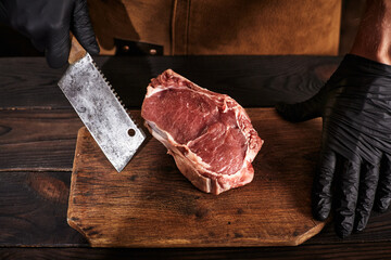 A butcher with a cleaver in black gloves and a leather apron holds a piece of meat.