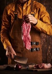 A butcher with a knife in a leather apron holds a piece of meat.