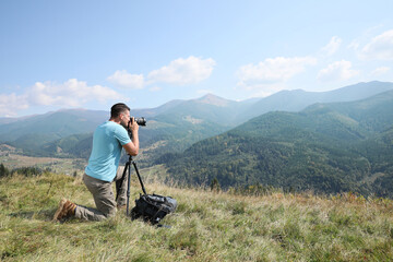 Professional photographer taking picture with modern camera in mountains. Space for text - obrazy, fototapety, plakaty