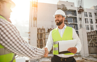 Engineers shaking hands at construction site - obrazy, fototapety, plakaty