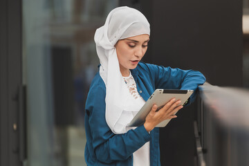 Smiling muslim girl using digital tablet, browsing Internet or social networks outdoor