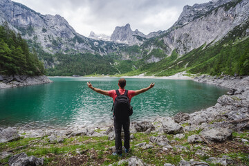 Naklejka na ściany i meble Happy traveler standing and admiring Dachstein peak mountains on a Upper Gosau Lake. Gosau, Salzkammergut, Austria, Europe