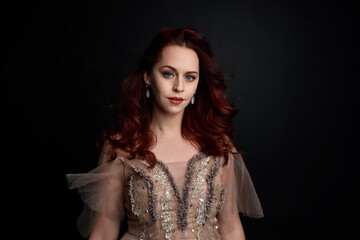 close up portrait of red haired  girl wearing a creamy fantasy gown like a fairy goddess costume.  isolated on dark studio background.
